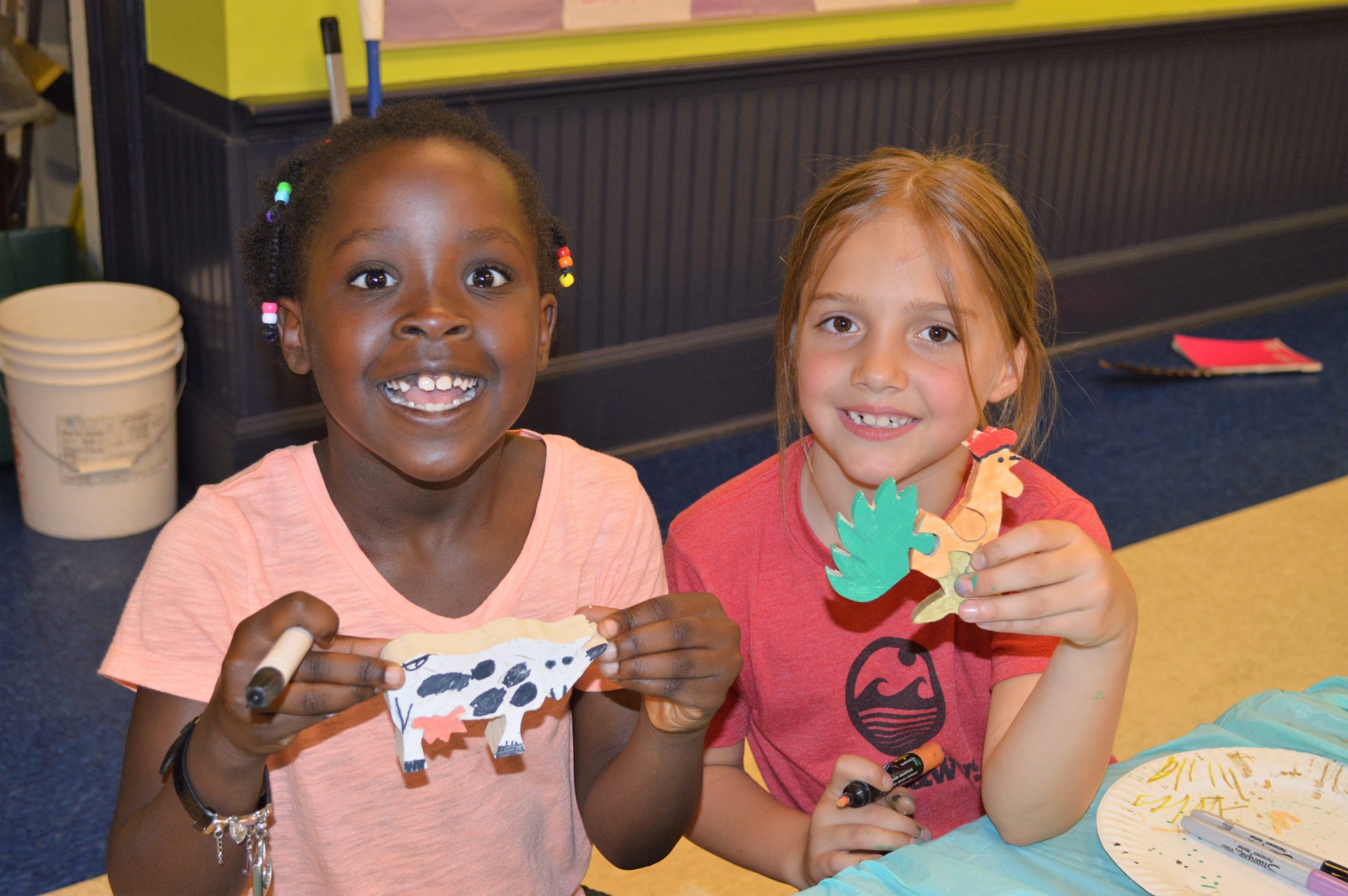 Two girls at a table, holding artwork they created