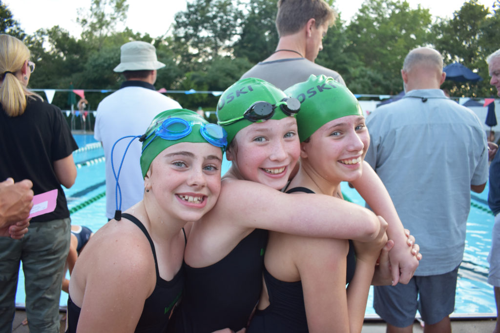 Three girls at edge of pool with Winooski Waves swim caps