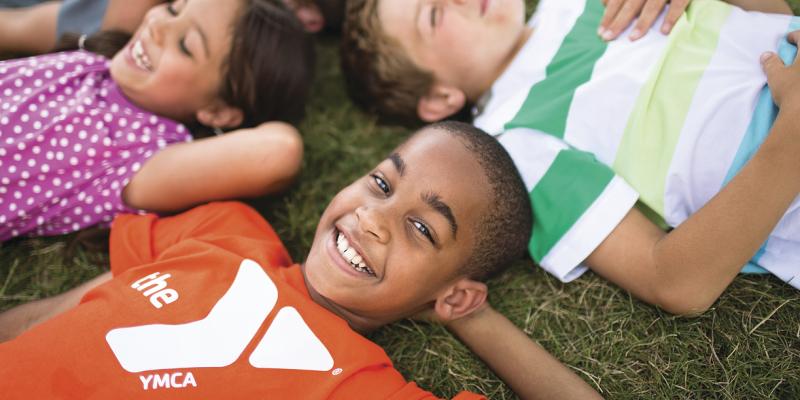 Diverse group of kids lying on backs on grass, smiling