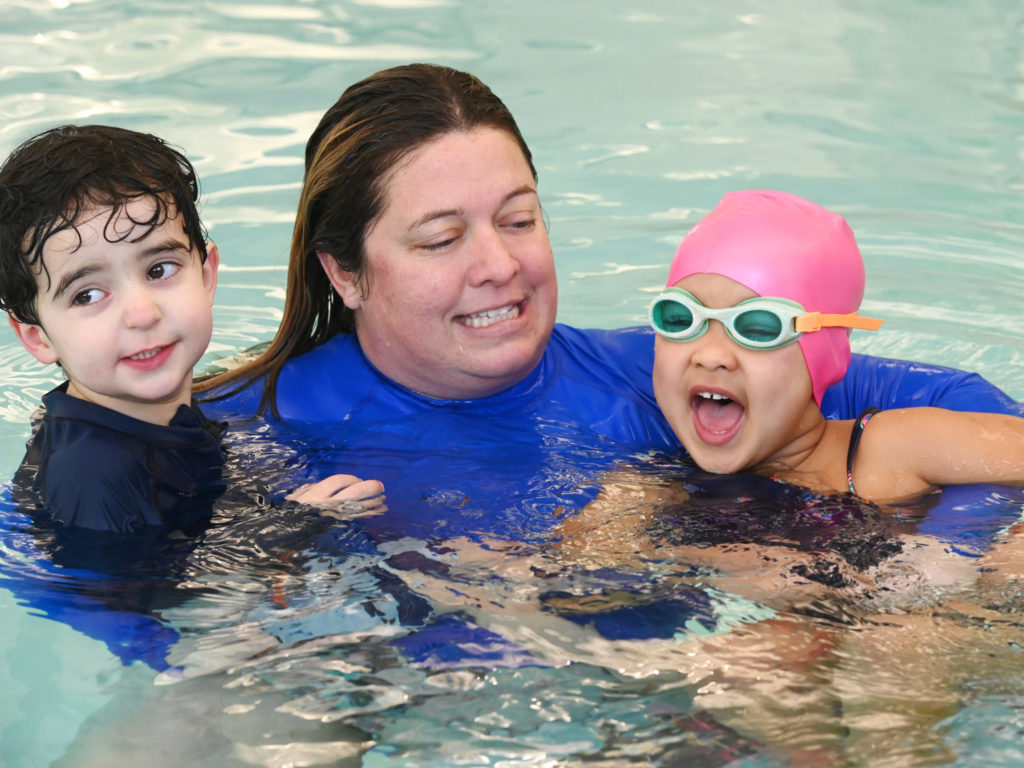 Swim instructor holding two kids in pool