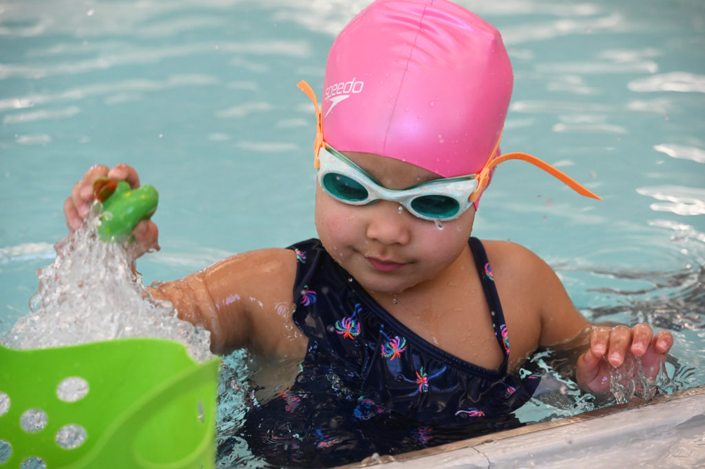 Young child in pool putting toys in basket