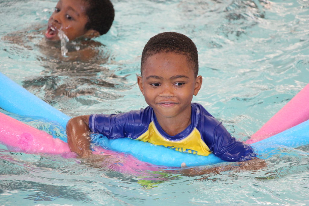 Boy swimming in pool holding noodles