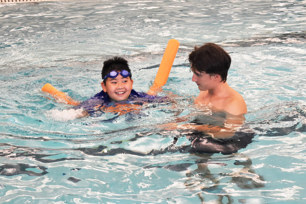 Swim instructor with boy with goggles and swim noodle in program pool