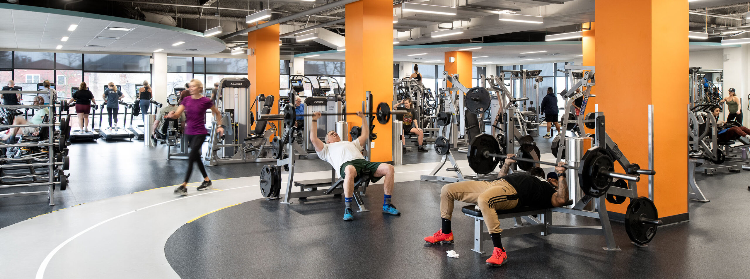 Overview of the GBYMCA wellness floor showing weight area, with cardio in the background and several people working out