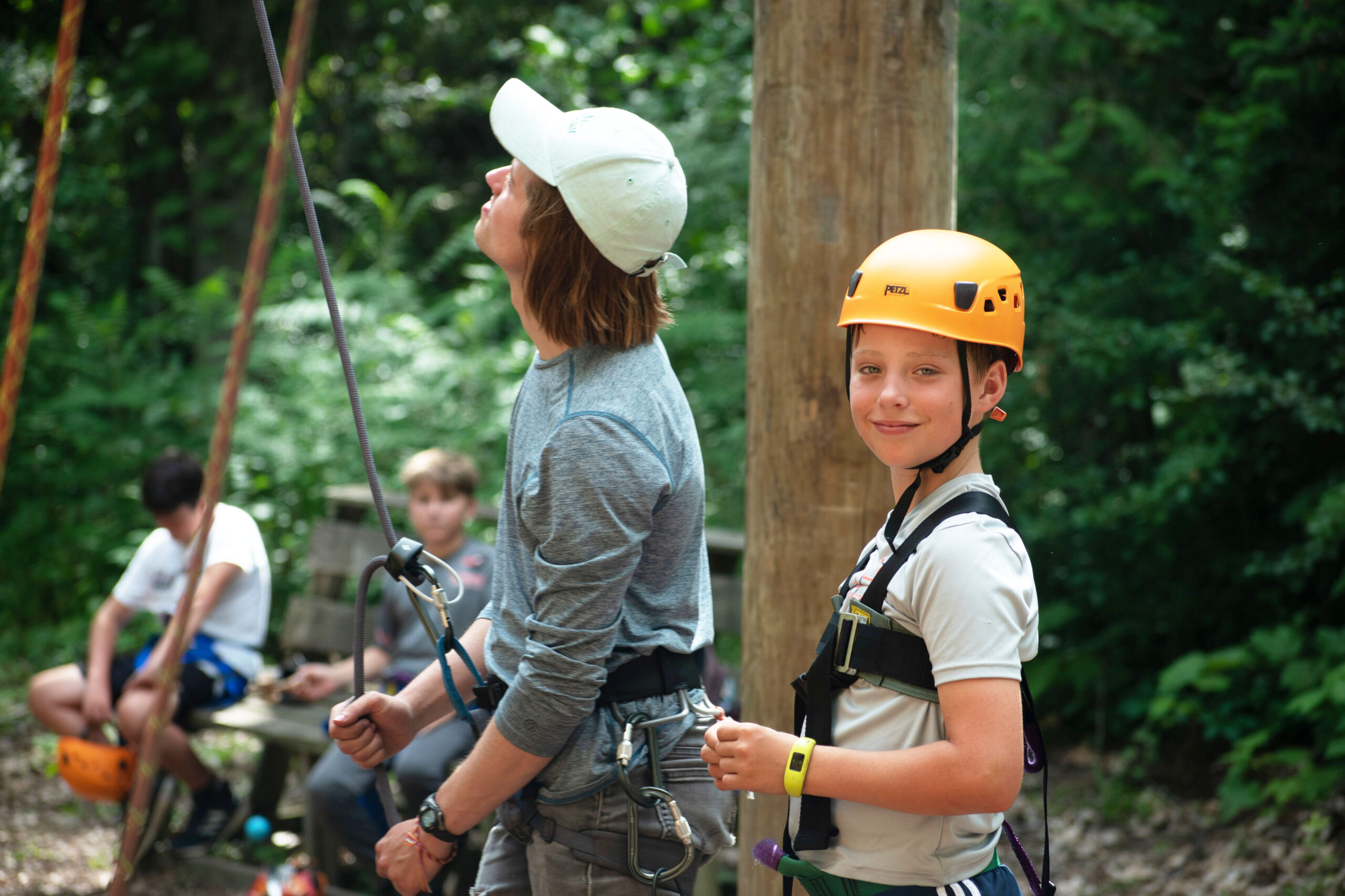 Young boy in climbing harness and helmet, awaiting his turn on the ropes course