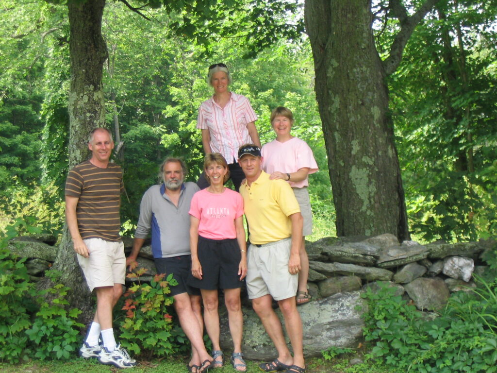 East Overshoe Aquatics Club members stand in a natural setting between two trees. Three people are lined up in front, two are being them, and one more is off to the left